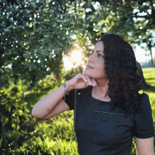 a woman in a black dress is standing in the grass looking up at the sun