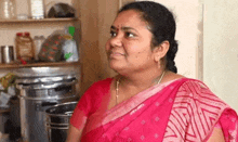 a woman in a pink sari is smiling and looking at the camera in a kitchen .