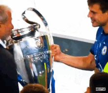 a man in a blue shirt is shaking hands with a man in a black shirt holding a trophy .