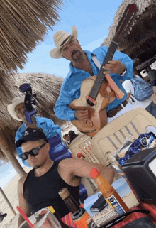 a man wearing a la hat sits at a table while another man plays a guitar