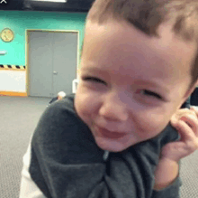 a little boy in a gray shirt is smiling and looking at the camera