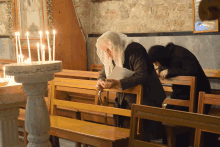 two women praying in a church with a candle holder that has arabic writing on it