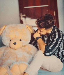 a man wearing a watch sits next to a giant teddy bear