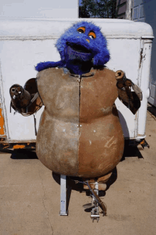 a blue stuffed animal with orange eyes is standing in front of a white box