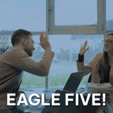 a man and a woman are giving each other a high five in front of a laptop with the words eagle five below them