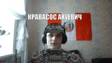 a man wearing a helmet and headphones stands in front of a flag that says kpabacoc