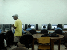 a man in a yellow shirt stands in front of a row of computer monitors