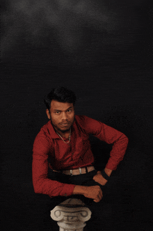 a young man in a red shirt sits on a pillar