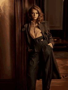 a woman in a trench coat is leaning against a doorway