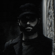 a man with a beard and hat is standing in the dark .