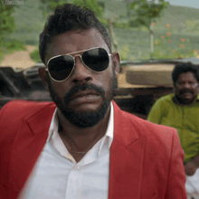 a man with a beard wearing sunglasses and a red jacket with the watermark toms 2005 on the bottom