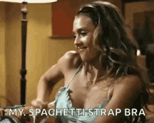 a woman in a bra is sitting on a couch and holding a spaghetti strap .