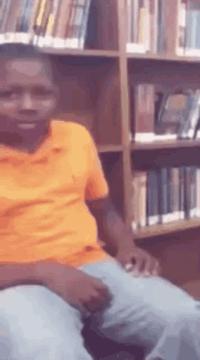 a man in an orange shirt is sitting in a library .