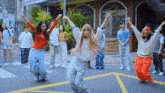 a group of young people are dancing on a street in front of a building with a no parking sign on it