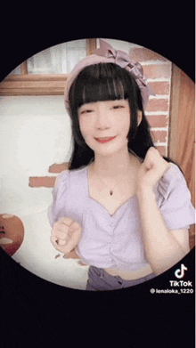 a woman wearing a purple top and a pink headband is making a heart shape with her hands .