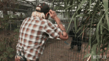 a man in a plaid shirt stands in front of a cage with a sign that says netflix on it