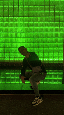 a man squatting in front of a wall of green blocks