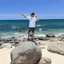 a man standing on a rock on a beach pointing to the ocean