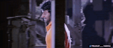 a man in an orange shirt is standing in a dark room with the hashtag pranay_varma