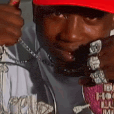 a man wearing a red hat and a lot of jewelry is giving a thumbs up sign .