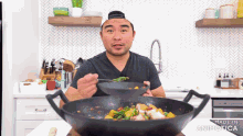 a man is eating food from a wok in a kitchen with the words made in animatica on the bottom