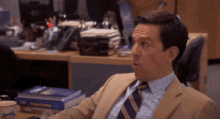 a man in a suit and tie is sitting at a desk in front of a stack of books .