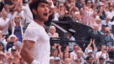 a man in a white shirt is standing in front of a crowd of people on a tennis court .