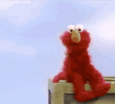 elmo from sesame street is sitting on a fence