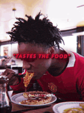 a man in a manchester united shirt is eating a slice of pizza