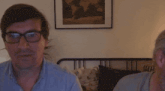 a man wearing glasses is smiling in front of a bed