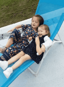 two little girls are laying on a blue chair holding hands