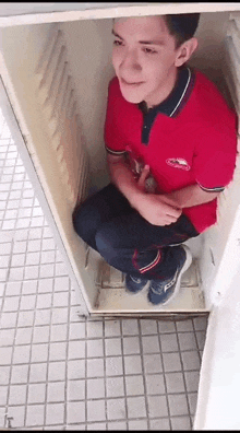 a young man in a red shirt is sitting inside of a locker .