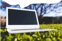 a white laptop is sitting on top of a lush green field .