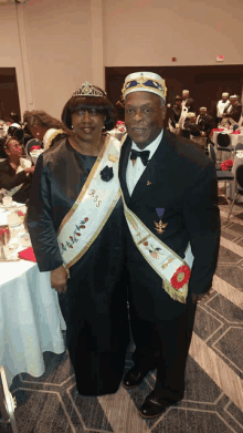 a man and a woman are posing for a picture and the woman is wearing a sash that says b & s on it