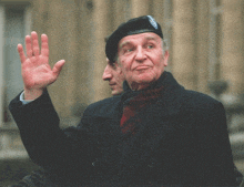 a man wearing a black beret waves his hand in front of a building