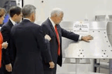 a group of men are standing around a table in a factory .