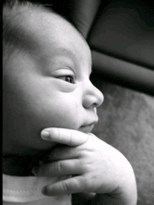 a black and white photo of a baby with a person holding his hand to his chin