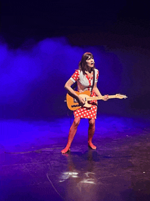 a woman in a polka dot dress is playing a guitar on stage