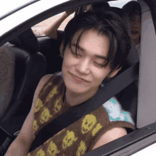 a young man wearing a vest with skulls on it is sitting in a car with his eyes closed