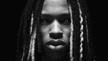 a black and white photo of a young man with dreadlocks looking at the camera