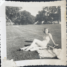 a black and white photo of a woman in a bathing suit laying on the grass