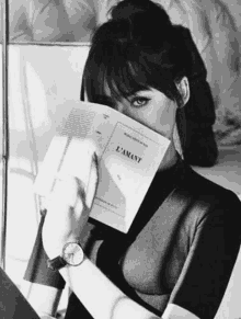 a black and white photo of a woman reading a book .