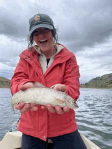 a woman in a red jacket is holding a fish and smiling