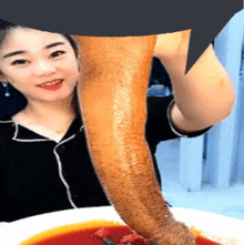 a woman is holding a very long piece of meat over a plate of soup