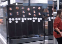 a woman in a red sweater is standing in front of a display of people 's faces on a wall