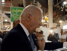 a man in a suit and tie is eating an ice cream cone at a market .