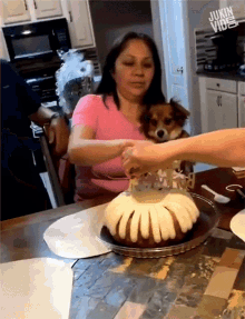 a woman is holding a small dog while a person cuts a cake with a sign that says happy birthday