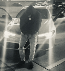 a man in a black hoodie stands in front of a white car