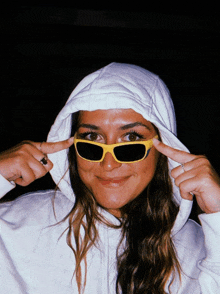 a woman wearing yellow sunglasses and a white hoodie is making a peace sign