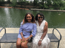 two women are sitting on a bench in front of a body of water